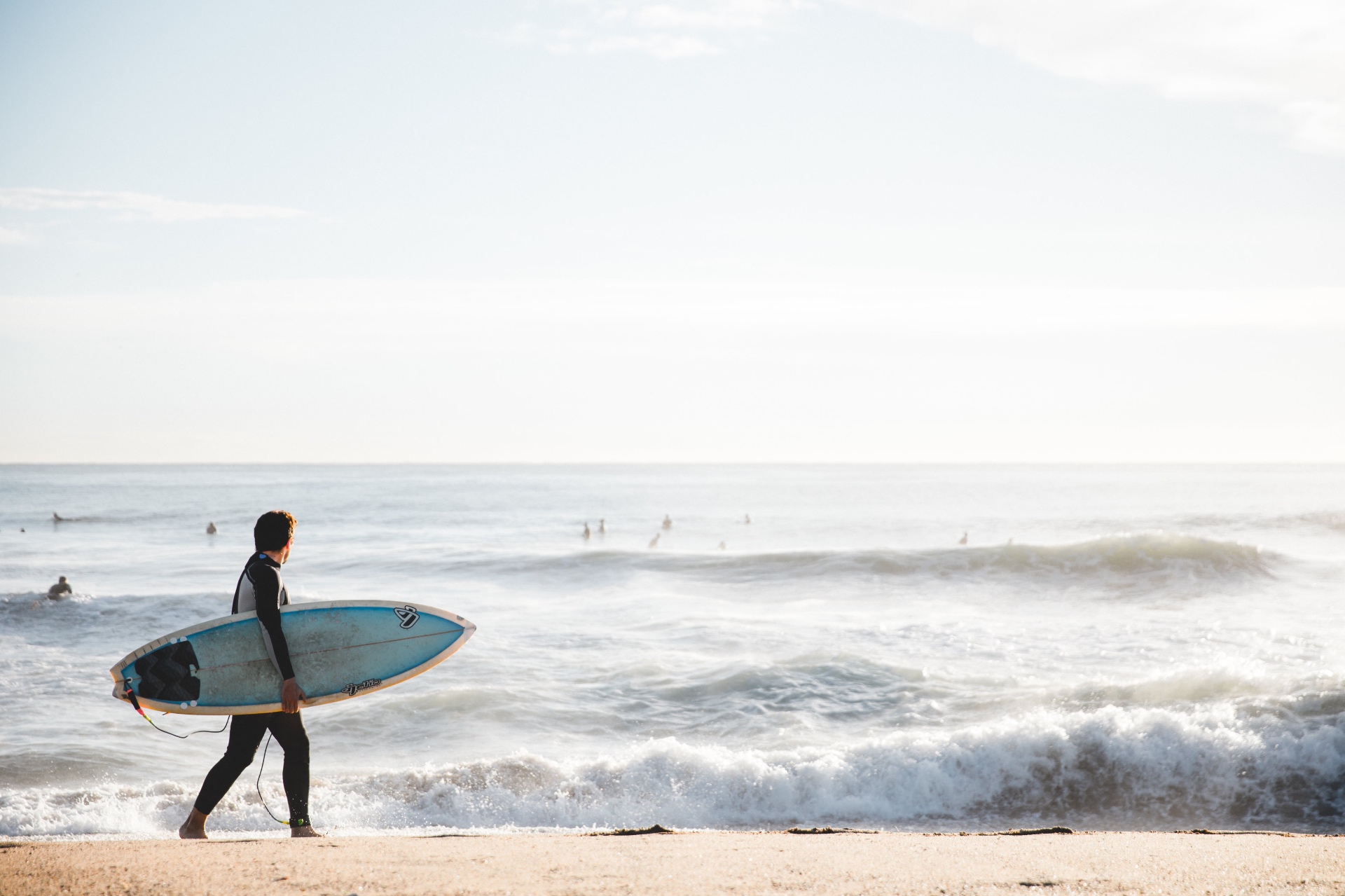 Surfer walking along a Rhode Island beach at golden hour